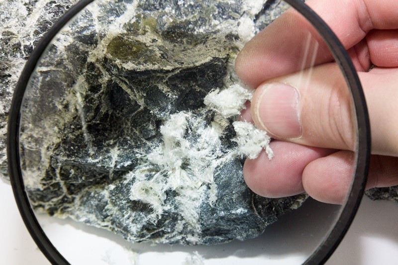 Hand with magnifying glass examines asbestos fibers in stone Asbestos removal SMART Environmental Services Kansas City AdobeStock_414466881