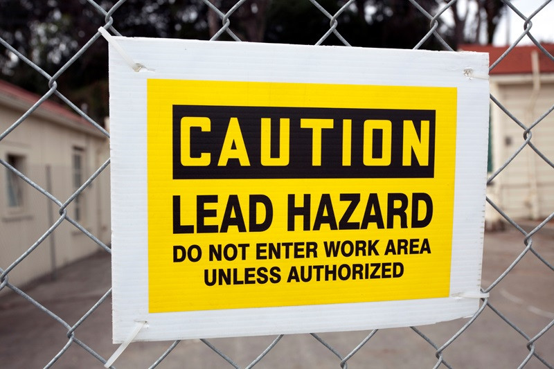 CAUTION LEAD HAZARD sign attached to chain link fence.