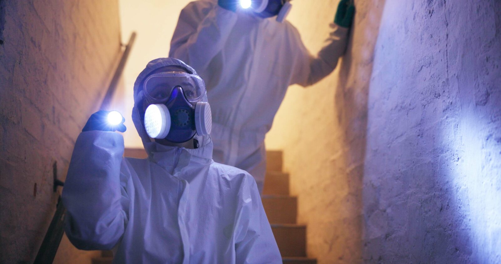 Hazmat, suit or people for safety walking with flashlight in basement for toxic spill or biohazard chemical inspection. Dark underground, forensic investigation or team with gas mask for disinfection AdobeStock_1041002368